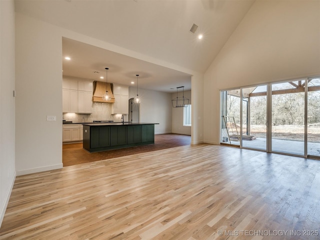 unfurnished living room featuring baseboards, recessed lighting, light wood-style flooring, high vaulted ceiling, and a sink