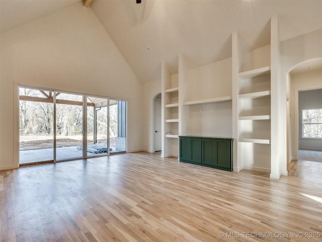 unfurnished living room with baseboards, built in features, light wood-style flooring, arched walkways, and high vaulted ceiling