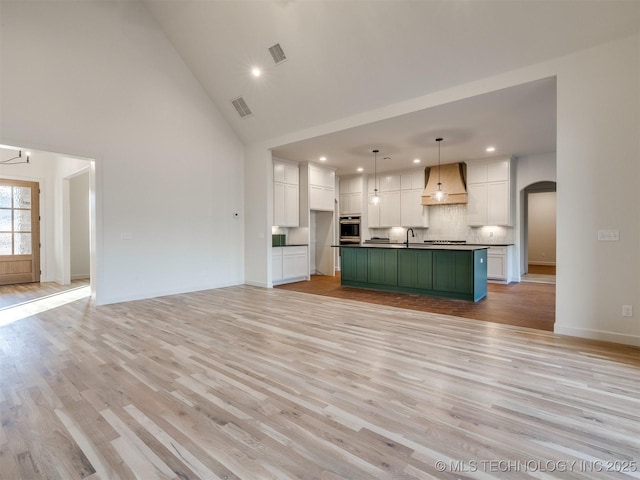 unfurnished living room with arched walkways, visible vents, light wood-style flooring, and a sink