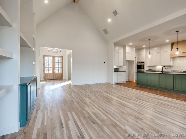 unfurnished living room featuring visible vents, light wood-style floors, high vaulted ceiling, and french doors