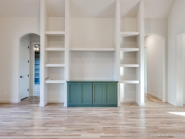 unfurnished living room with built in features, light wood-type flooring, arched walkways, and baseboards