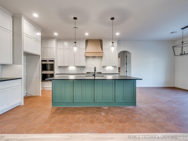 kitchen with premium range hood, a sink, dark countertops, double oven, and white cabinets