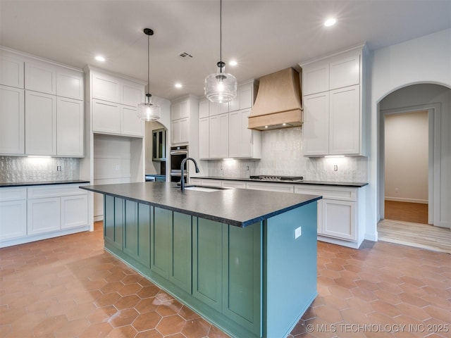 kitchen featuring dark countertops, arched walkways, stainless steel gas stovetop, custom exhaust hood, and a sink