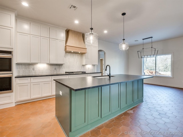 kitchen featuring custom exhaust hood, stovetop, arched walkways, a sink, and dark countertops