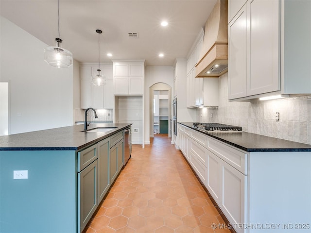 kitchen with custom exhaust hood, arched walkways, a sink, stainless steel appliances, and dark countertops