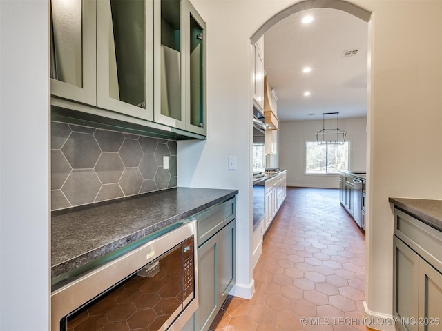 kitchen featuring oven, dark countertops, glass insert cabinets, arched walkways, and decorative backsplash