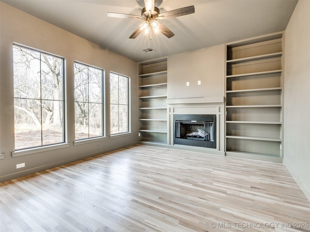 unfurnished living room featuring visible vents, built in shelves, a fireplace, wood finished floors, and a ceiling fan