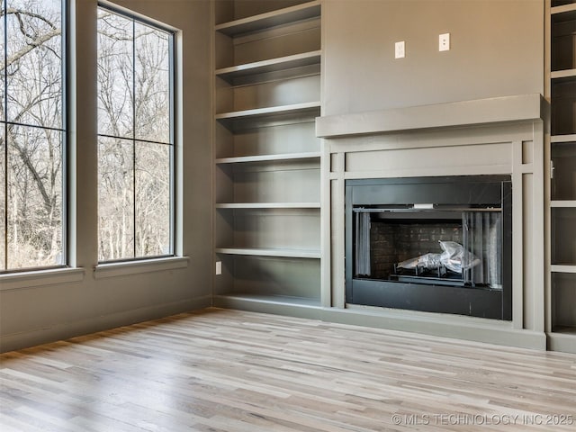 unfurnished living room featuring built in shelves, a fireplace, and wood finished floors