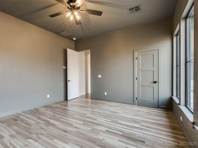 empty room featuring light wood-style flooring, a ceiling fan, visible vents, and baseboards