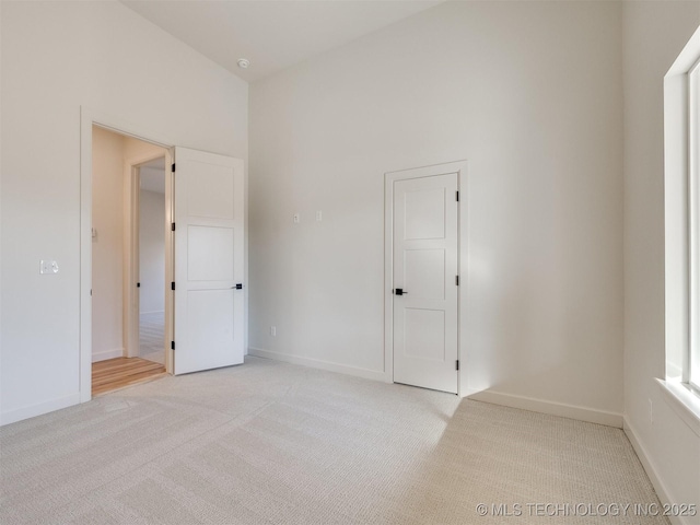 unfurnished bedroom featuring light carpet, baseboards, and a towering ceiling