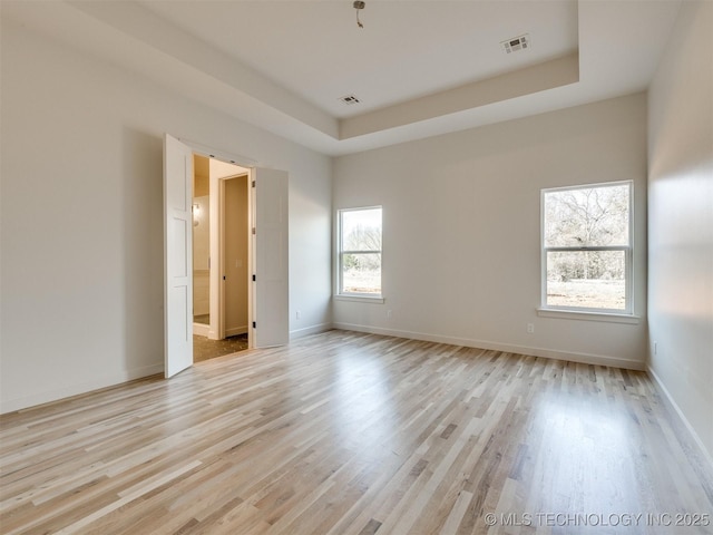 unfurnished room featuring a tray ceiling, visible vents, baseboards, and light wood finished floors