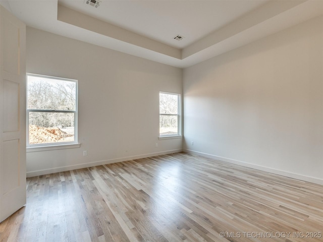 unfurnished room with a raised ceiling, visible vents, baseboards, and light wood finished floors