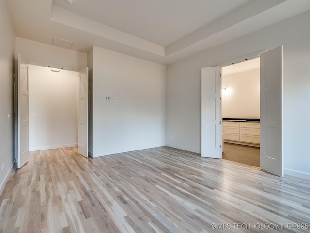 unfurnished room featuring light wood finished floors, a tray ceiling, and baseboards