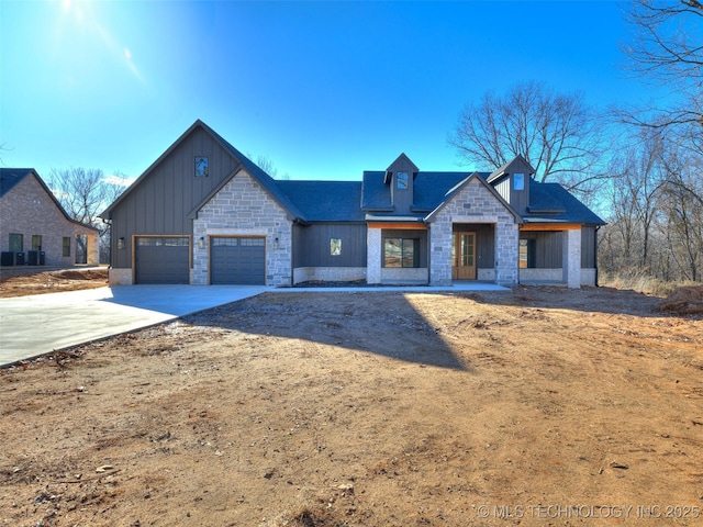 view of front of property with board and batten siding, a garage, stone siding, and driveway