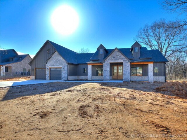 view of front of property featuring driveway, an attached garage, french doors, stone siding, and board and batten siding