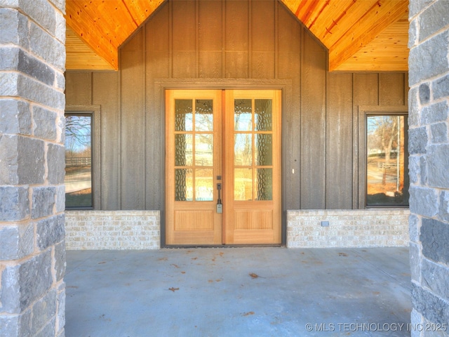 view of exterior entry with board and batten siding and a patio