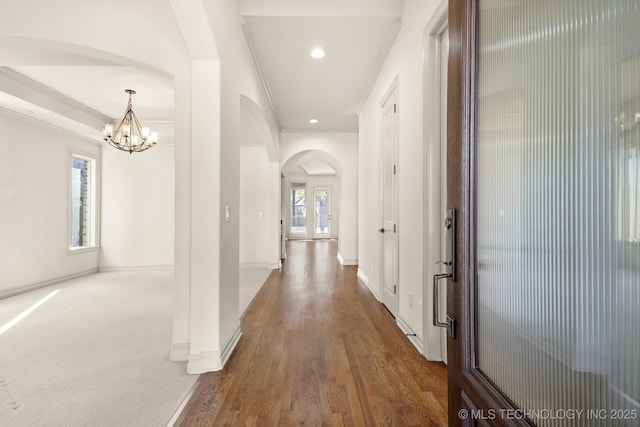 hallway featuring arched walkways, a wealth of natural light, crown molding, and an inviting chandelier
