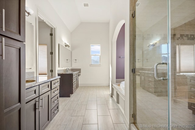 bathroom featuring lofted ceiling, a sink, visible vents, a stall shower, and two vanities