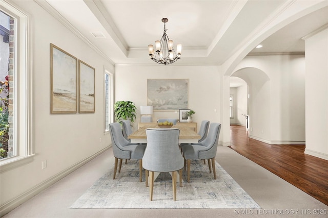 dining space featuring hardwood / wood-style flooring, a tray ceiling, ornamental molding, and a notable chandelier