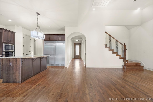 kitchen with a kitchen breakfast bar, dark brown cabinets, decorative light fixtures, light stone counters, and built in appliances