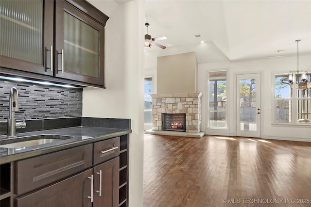 kitchen with dark stone counters, a stone fireplace, sink, hanging light fixtures, and dark brown cabinets