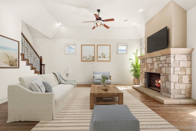 living area with a fireplace, ceiling fan, vaulted ceiling, baseboards, and wood finished floors