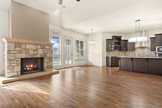 unfurnished living room with crown molding, a fireplace, sink, dark wood-type flooring, and ceiling fan with notable chandelier