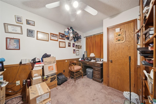 carpeted home office featuring wooden walls, a textured ceiling, and ceiling fan