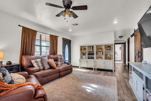 living room featuring a barn door, ceiling fan, and light hardwood / wood-style flooring