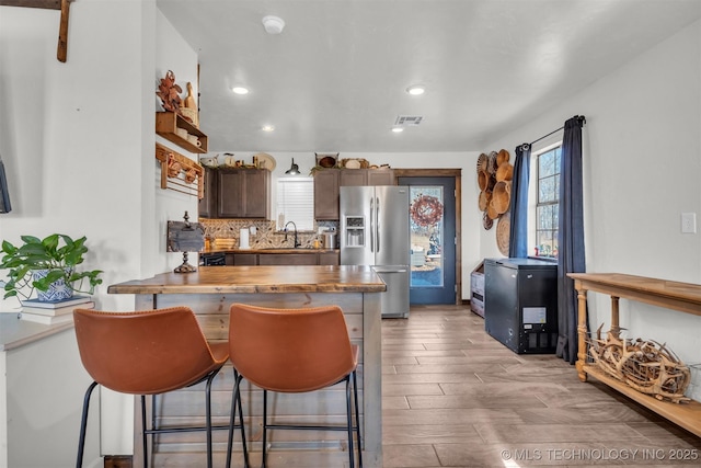 kitchen featuring wood counters, tasteful backsplash, sink, a breakfast bar area, and stainless steel refrigerator with ice dispenser