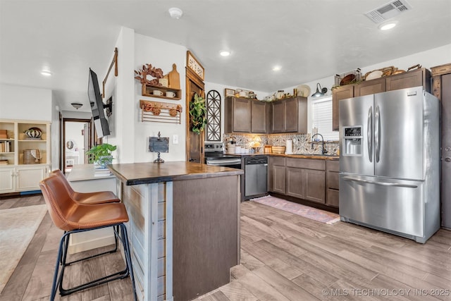 kitchen with sink, appliances with stainless steel finishes, dark brown cabinets, light hardwood / wood-style floors, and a kitchen bar