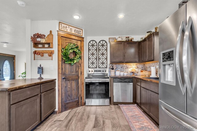 kitchen with dark brown cabinetry, light hardwood / wood-style flooring, appliances with stainless steel finishes, kitchen peninsula, and backsplash