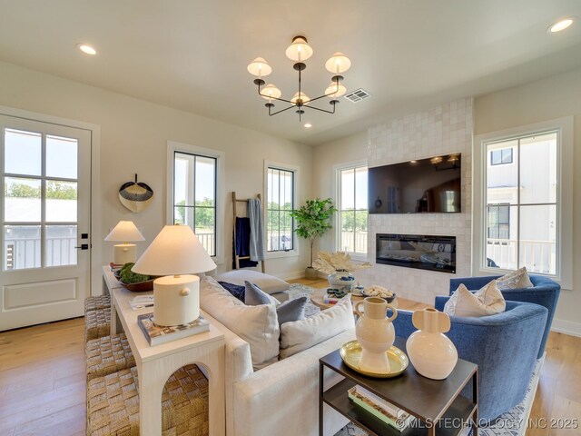 living room featuring a tiled fireplace, a notable chandelier, light hardwood / wood-style floors, and a healthy amount of sunlight