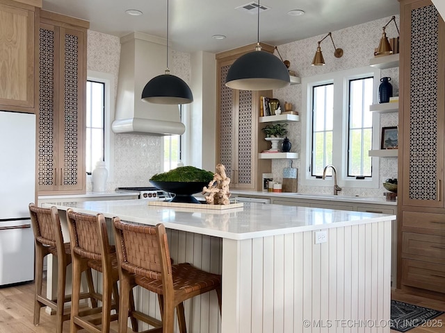 kitchen featuring a kitchen island, tasteful backsplash, white refrigerator, custom range hood, and light hardwood / wood-style flooring