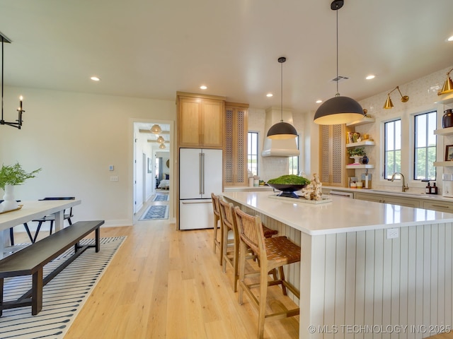 kitchen with high end fridge, sink, light wood-type flooring, a kitchen island, and pendant lighting