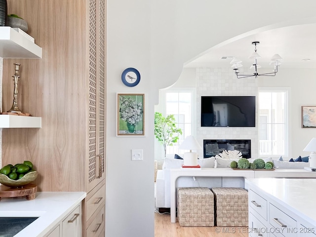 kitchen featuring a large fireplace, white cabinets, a chandelier, hanging light fixtures, and light wood-type flooring