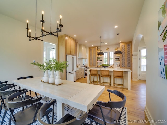 dining area featuring arched walkways, recessed lighting, baseboards, and light wood-style floors