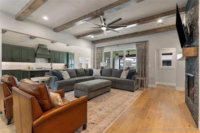 living room featuring beam ceiling, ceiling fan, a fireplace, and light hardwood / wood-style floors