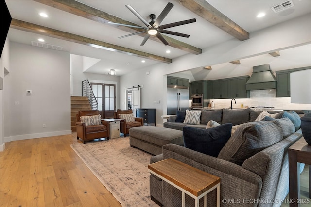 living room featuring beamed ceiling, sink, ceiling fan, a barn door, and light hardwood / wood-style flooring