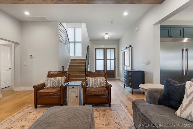 living room featuring a barn door, beam ceiling, and light wood-type flooring