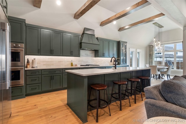 kitchen featuring pendant lighting, light hardwood / wood-style flooring, appliances with stainless steel finishes, a kitchen island with sink, and custom exhaust hood