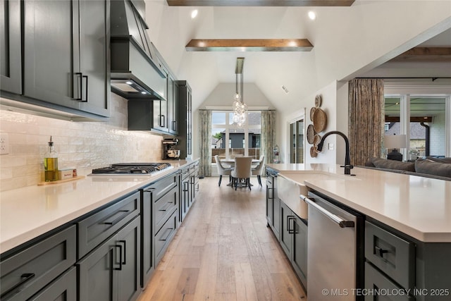 kitchen with appliances with stainless steel finishes, sink, light hardwood / wood-style floors, hanging light fixtures, and decorative backsplash