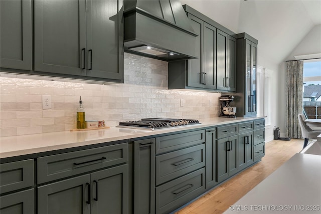 kitchen with lofted ceiling, backsplash, light hardwood / wood-style floors, stainless steel gas cooktop, and custom exhaust hood