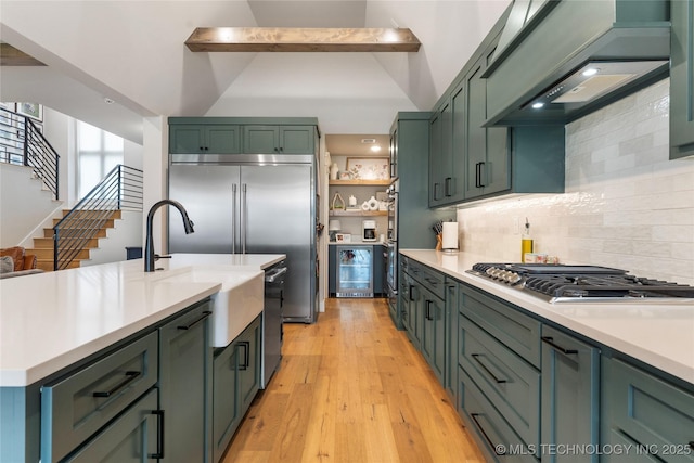 kitchen with green cabinets, stainless steel appliances, light hardwood / wood-style floors, custom exhaust hood, and beverage cooler