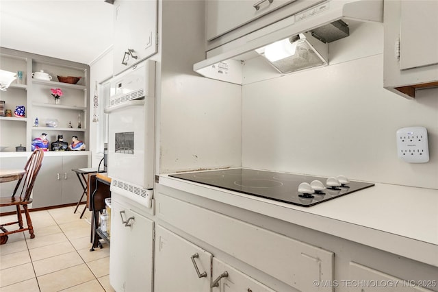 kitchen featuring oven, custom range hood, black electric cooktop, white cabinets, and light tile patterned flooring