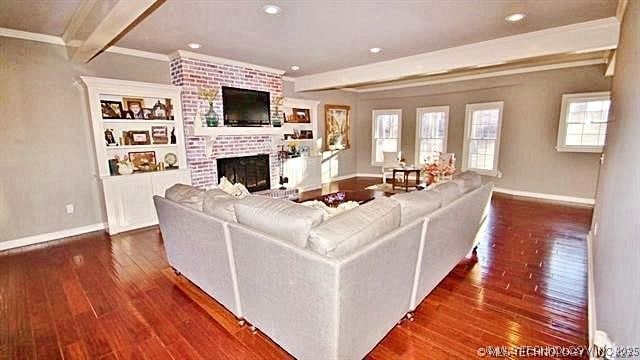 living room with a brick fireplace, dark hardwood / wood-style flooring, crown molding, and beamed ceiling