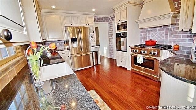 kitchen with dark hardwood / wood-style floors, custom range hood, dark stone counters, and high end appliances