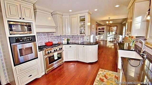 kitchen with custom exhaust hood, stainless steel appliances, an inviting chandelier, decorative backsplash, and kitchen peninsula