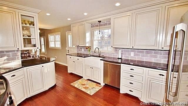 kitchen with stainless steel dishwasher, sink, white cabinets, dark hardwood / wood-style flooring, and backsplash