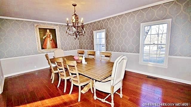 dining area with dark wood-type flooring, a healthy amount of sunlight, crown molding, and an inviting chandelier